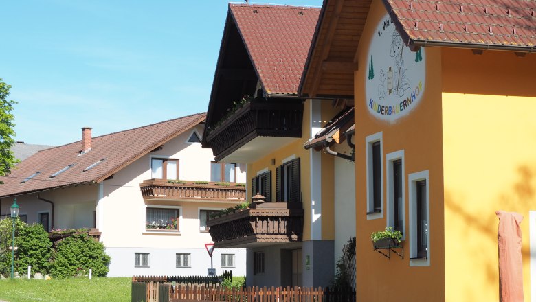 Waldviertel children's farm building with yellow fa&ccedil;ade and wooden balconies, surrounded by green countryside.
