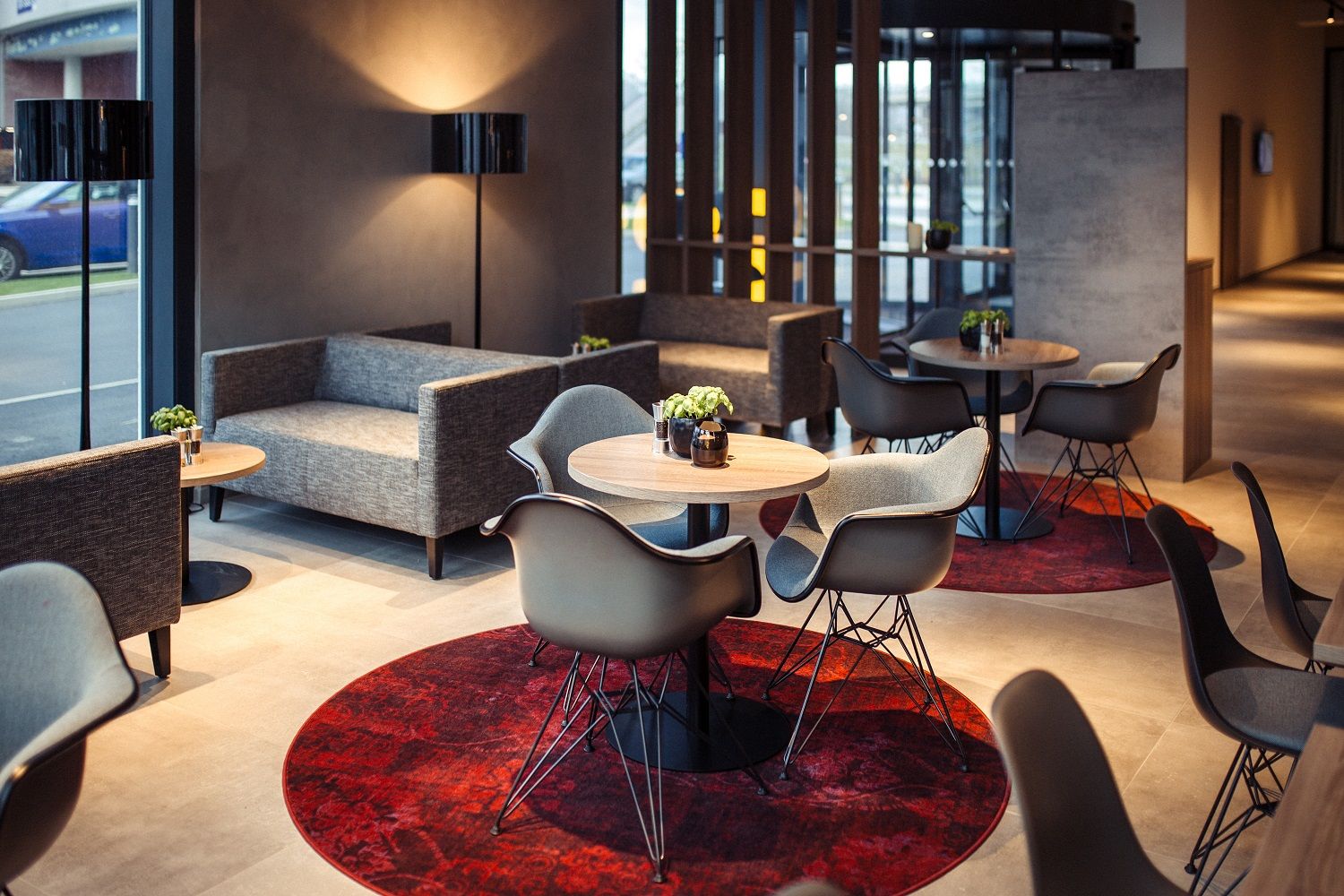 Modern hotel lobby with gray sofas, round wooden tables and red carpets.