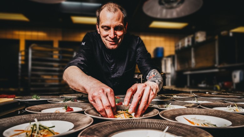 A cook in a black uniform carefully arranges food on several plates.