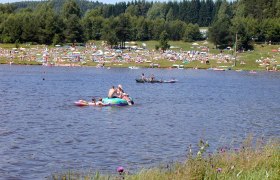 People relax by the Frauenwieserteich pond with sun loungers and parasols.