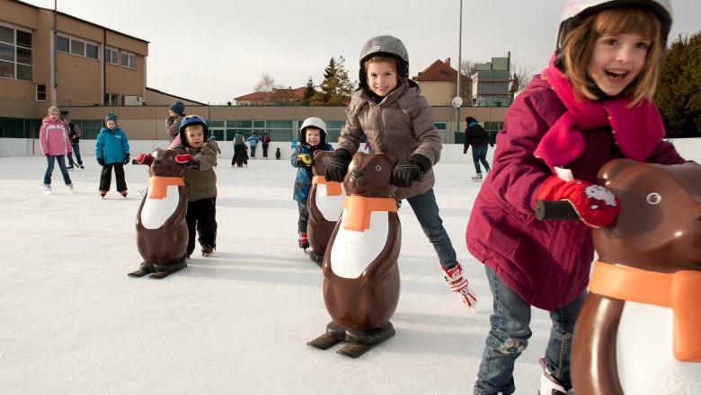 Children skating with penguin aids on an ice rink.