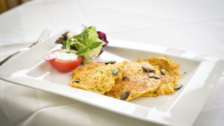 A plate of potato pancakes, pumpkin seeds and salad on a white table.