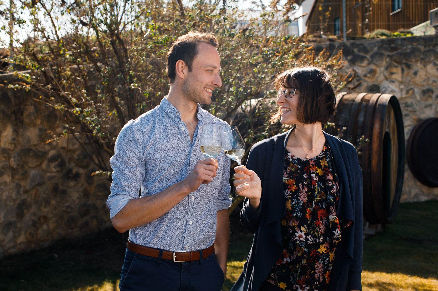 A man and a woman clink glasses of wine outside.