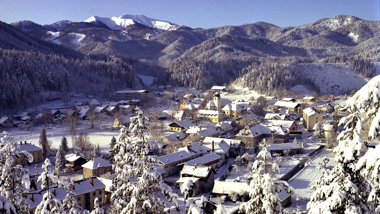 Winter landscape of St. Aegyd with snow-covered houses and mountains in the background.