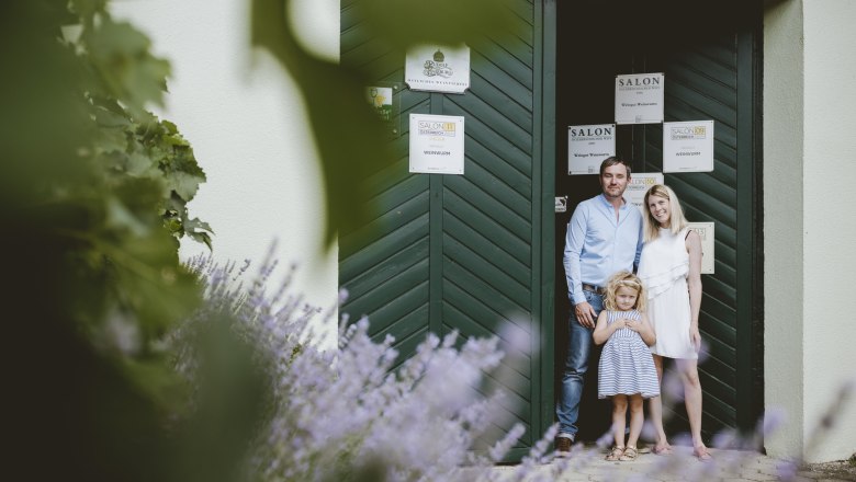 A family stands in front of a green gate, surrounded by lavender and plants.