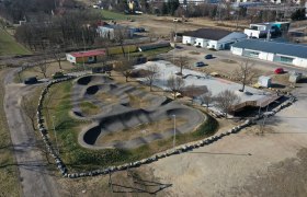 Aerial view of a pump track with surrounding buildings and parking lots.