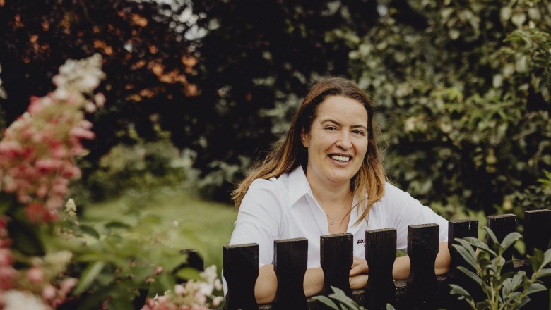 Woman in white shirt smiling behind a wooden fence in the garden.