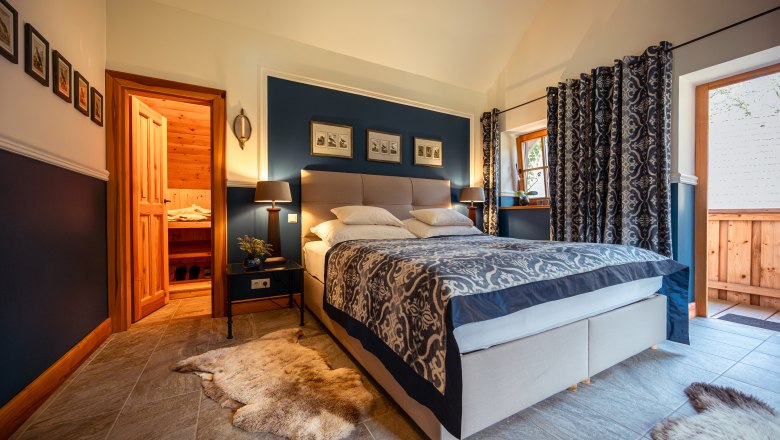 Cozy bedroom with double bed, blue walls and wooden elements, adjacent to a sauna.