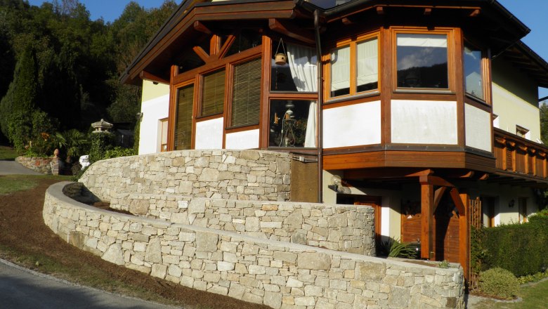 House view, © Kesper House with stone wall and wooden cladding, surrounded by trees.