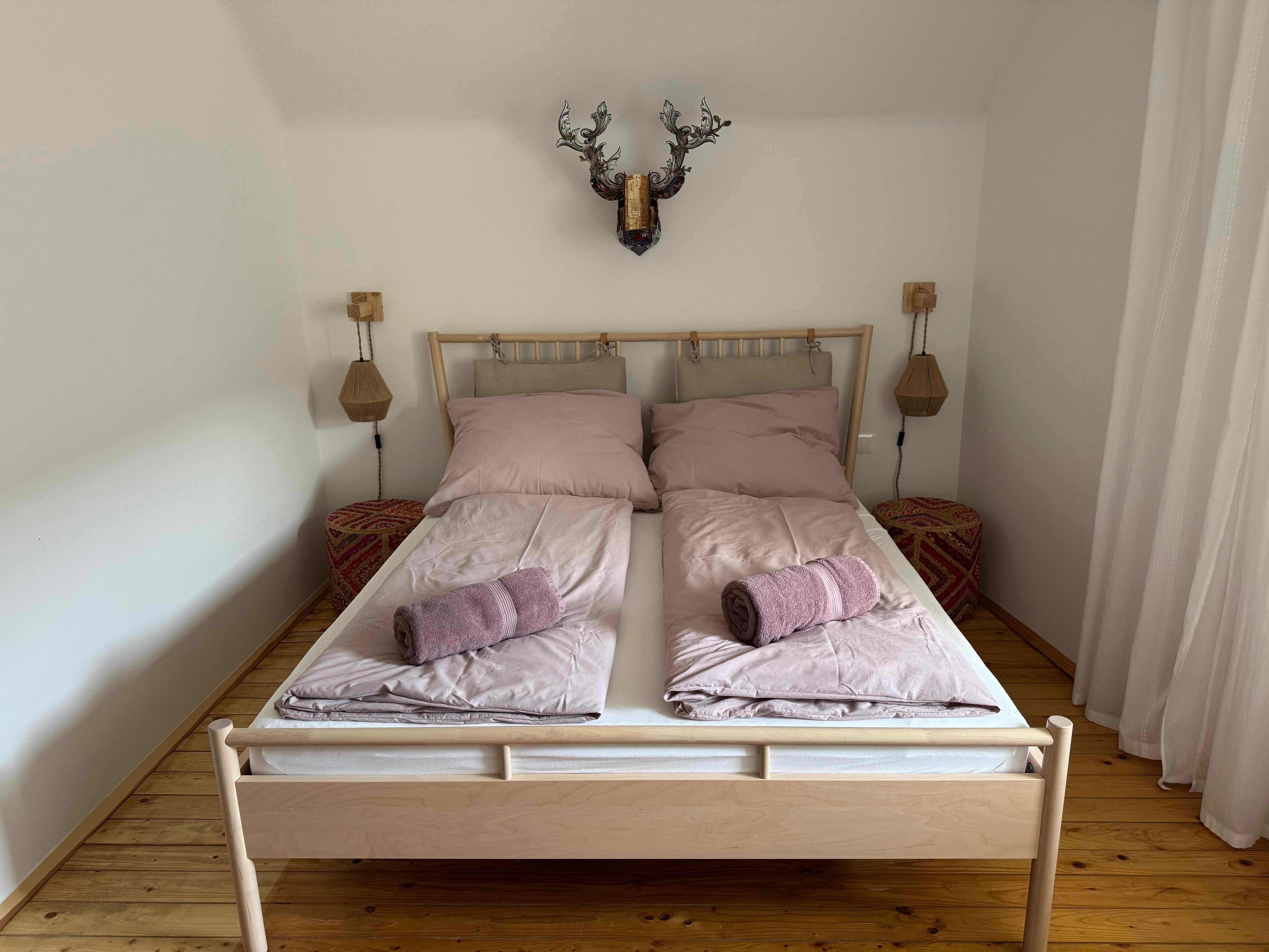 Bedroom with double bed, pink bed linen and towels, wooden floor and wall decoration.