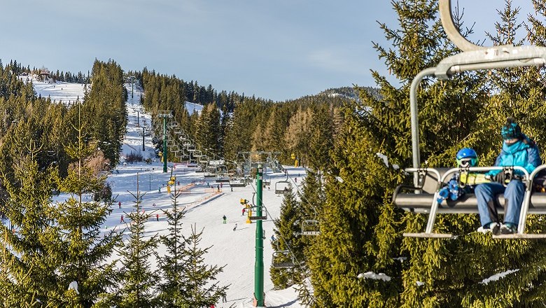 Ski area with chair lift and skiers, surrounded by snow-covered trees.