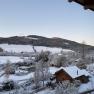 Winter landscape with snow-covered hills and a wooden house in the foreground.