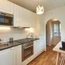Modern kitchen with white cupboards, wooden floor and appliances such as oven and microwave.