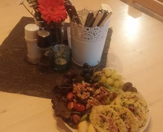 A plate of cold cuts, nuts, grapes and bread on a table with flowers and spices.
