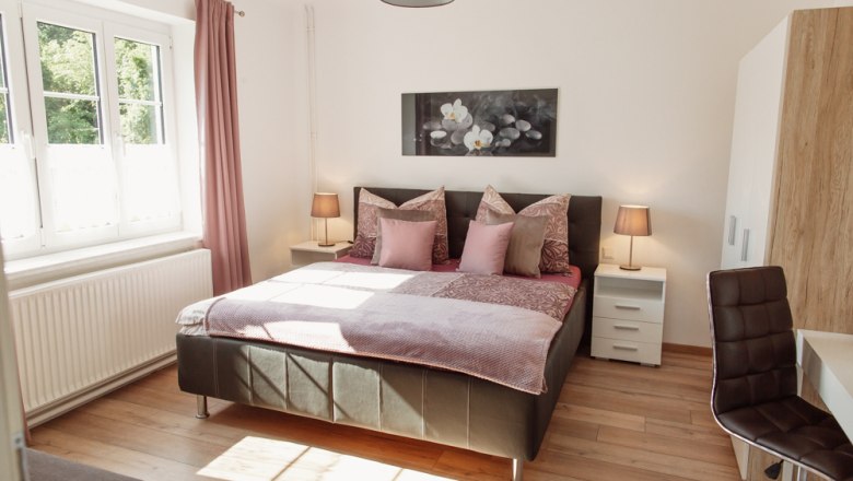 Bright bedroom with double bed, two bedside tables and a window with pink curtains.