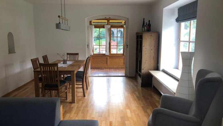 A living room with wooden floor, dining table, chairs, armchair and window with a view outside.