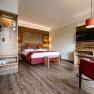 Modern hotel room with double bed, wooden furniture and red armchair.