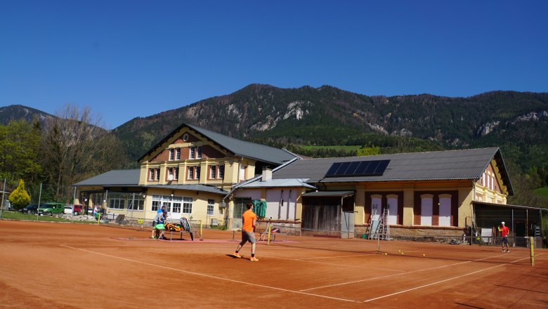 Tennis court in front of a building with mountains in the background.