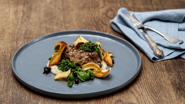 Gourmet dish with meat, mushrooms and kale on a gray plate.