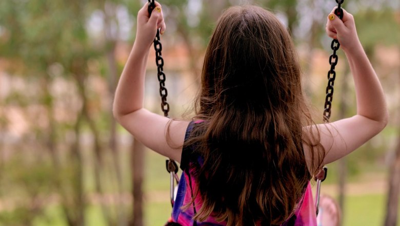 A child swings outdoors, photographed from behind, surrounded by trees.