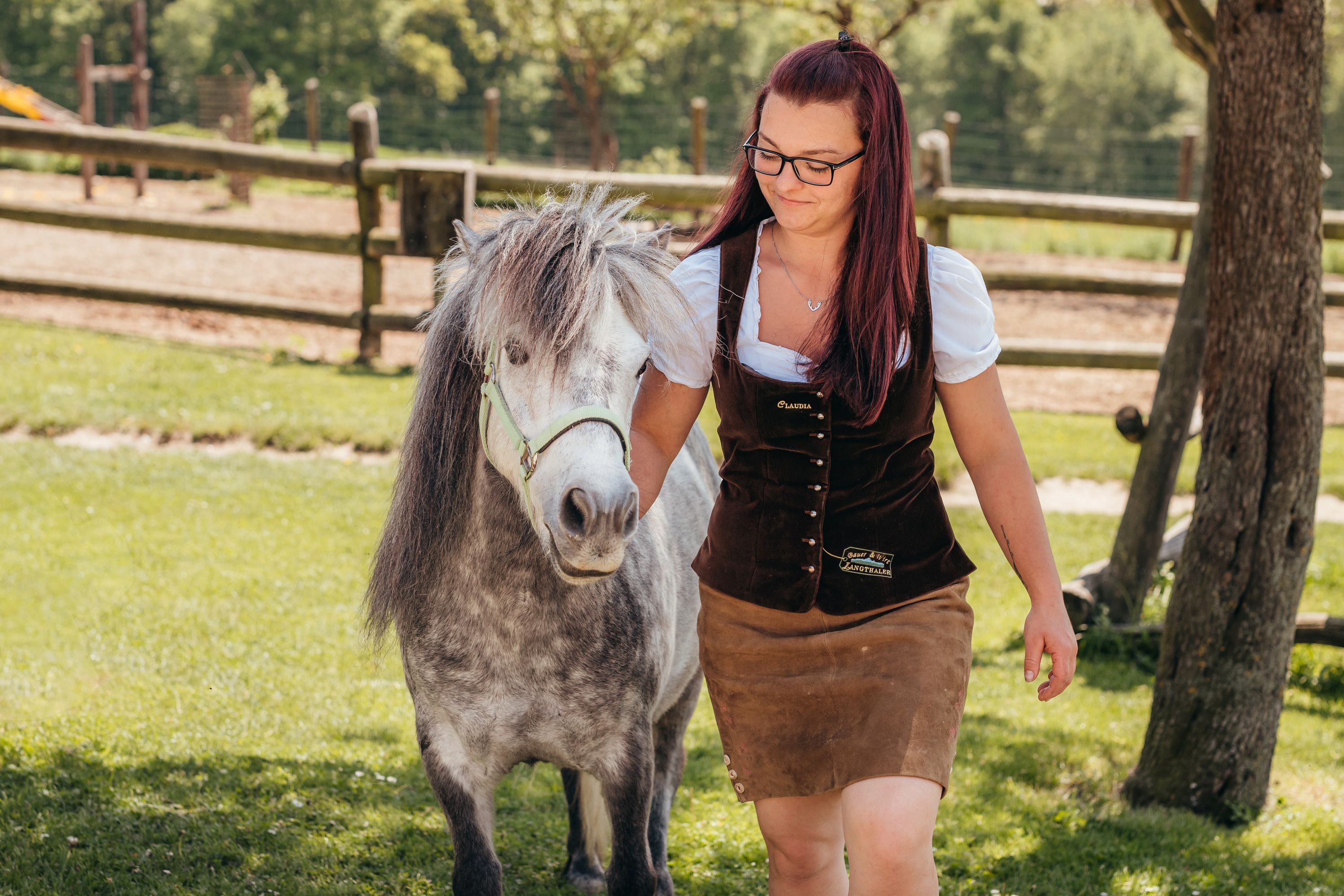 Claudia Langthaler leads a pony in a meadow, with a wooden fence in the background.