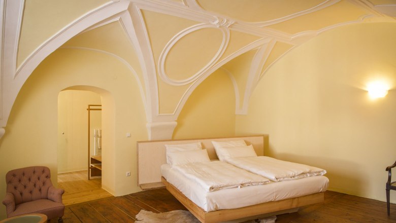 An elegant bedroom with a vaulted ceiling, a double bed, an armchair and wooden floor.