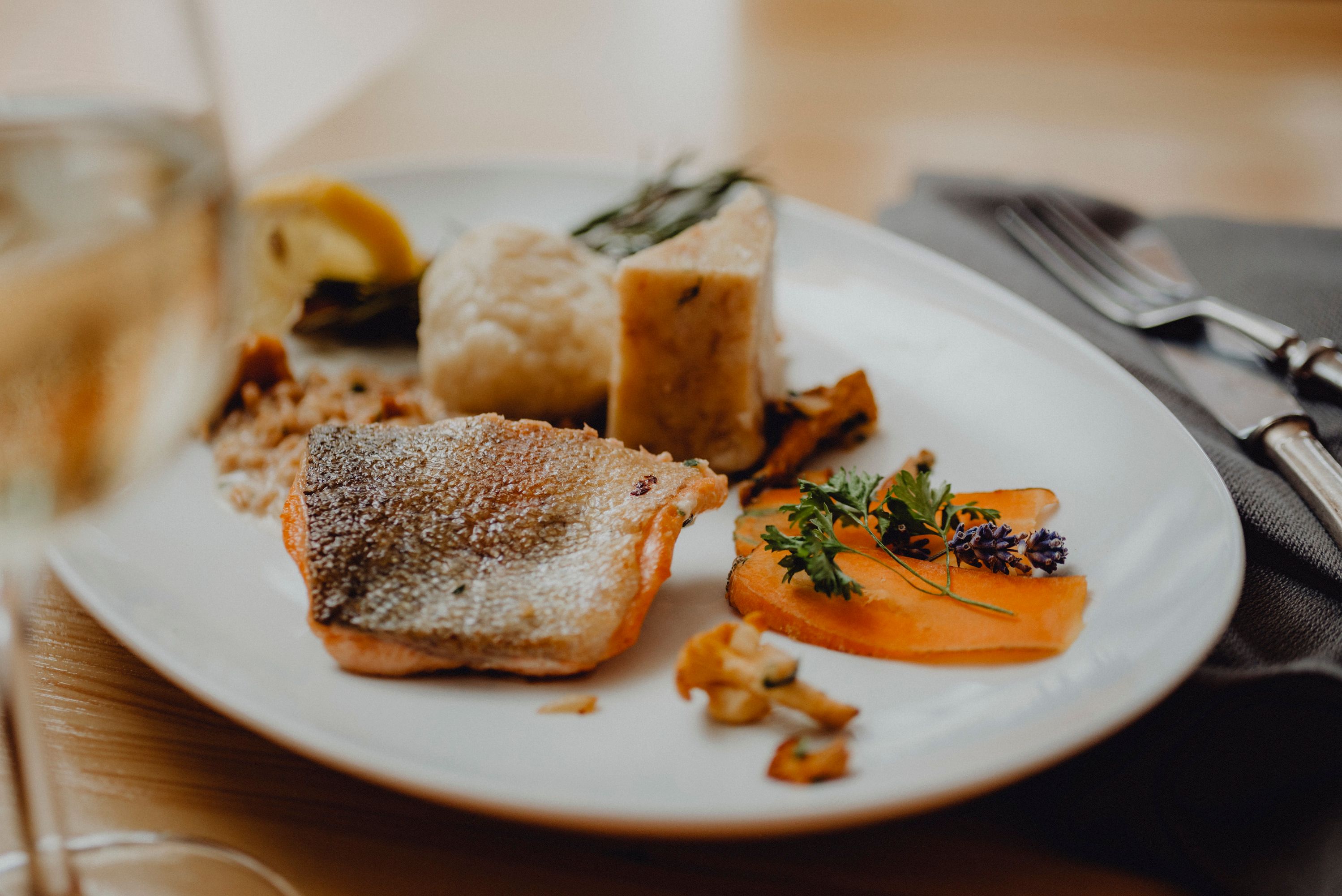 A plate of fried char, porcini mushroom dumplings and vegetables, decorated with herbs.