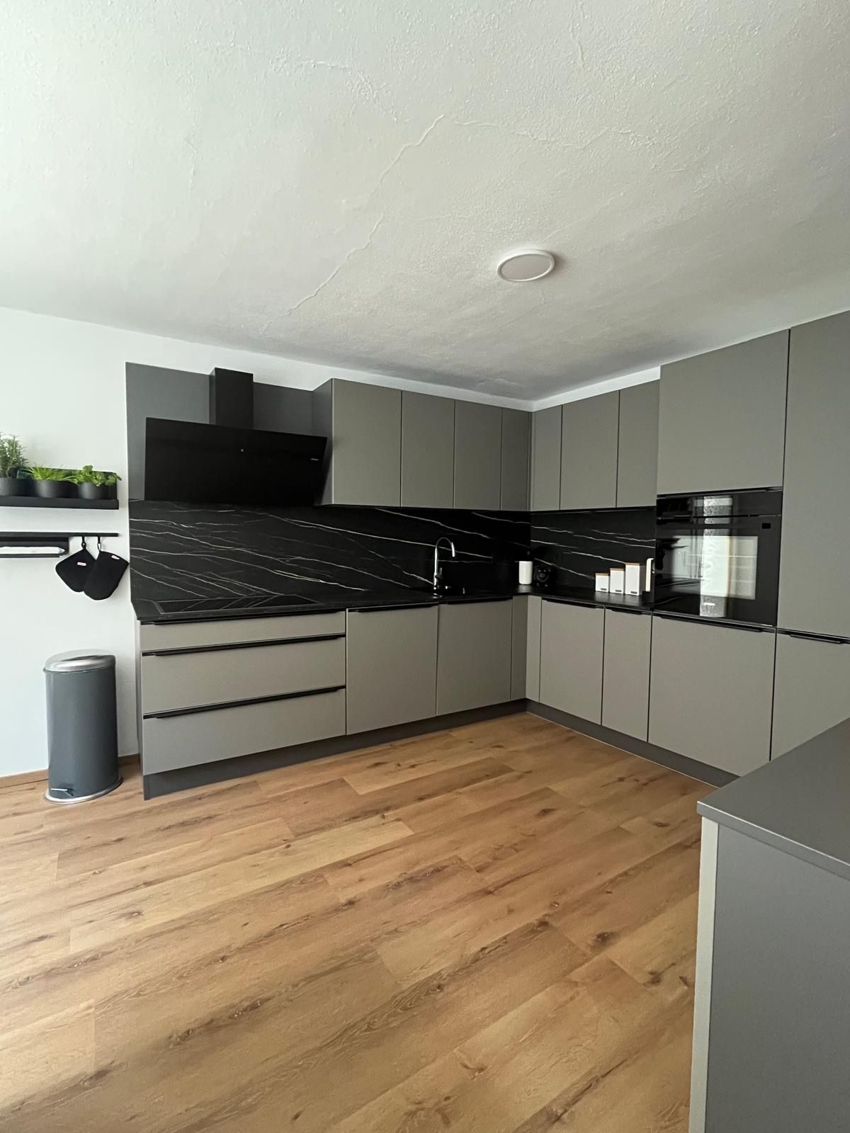 Modern gray kitchen unit with black worktops and wooden floor.