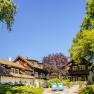 A traditional country house with a wooden roof and blue deckchairs in the garden, surrounded by trees and blue skies.