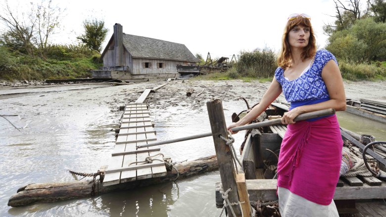 Woman on a boat in front of a ship mill on a river bank.