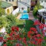 View of a garden with pool, surrounded by houses and red flowers in the foreground.