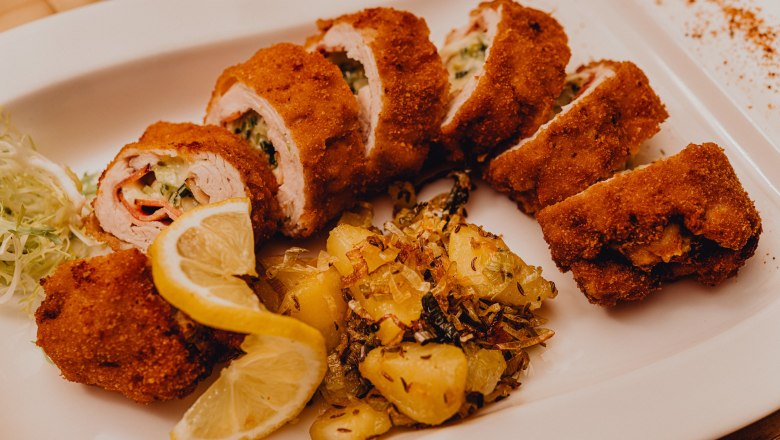 Stuffed baked turkey fillet with potato garnish and lemon slices on a white plate.