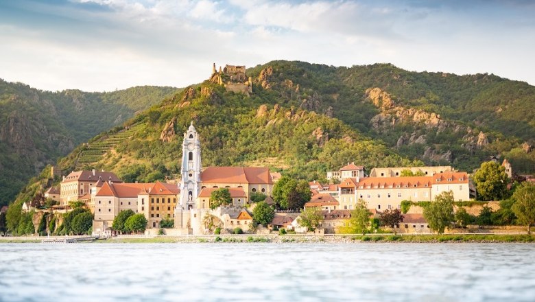 View of D&uuml;rnstein with monastery and castle ruins in front of wooded hills.