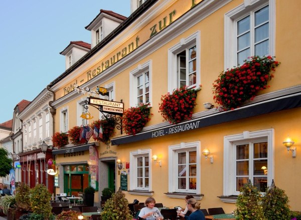 Facade of a yellow building with the lettering 'Hotel-Restaurant zur Post'. People are sitting at tables in front of the building.