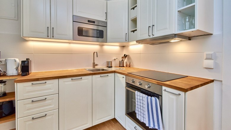 Modern kitchen with white cupboards, wooden worktops, stove and sink.