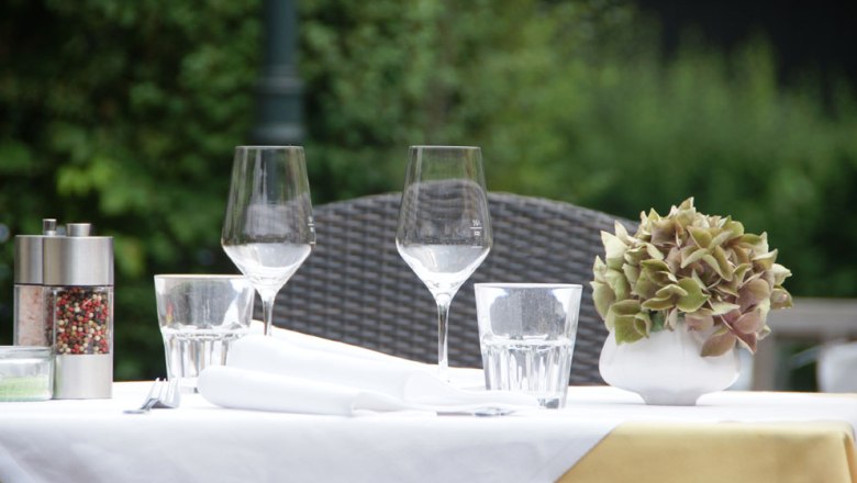 Outdoor table setting with wine glasses, water glasses, pepper mill and floral decorations.