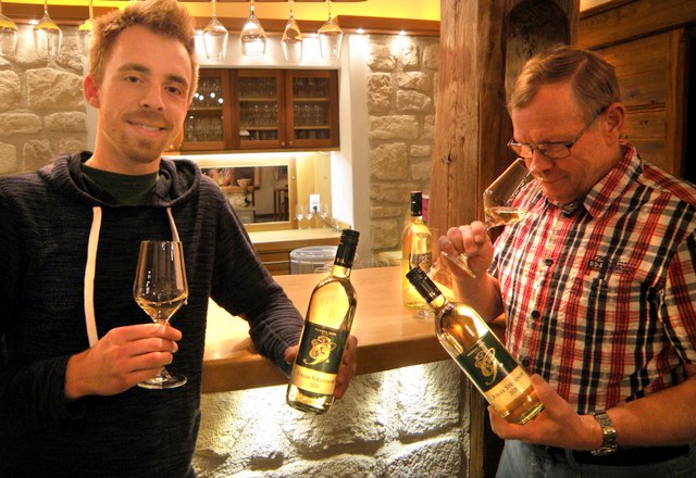 Two men in a wine bar holding wine glasses and bottles of wine.