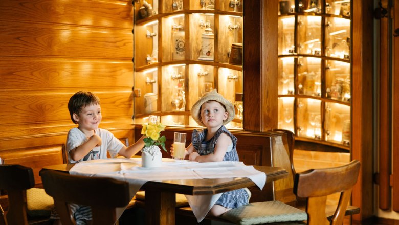 Two children sit at a table in a wood-paneled restaurant.