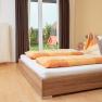 A cozy bedroom with a double bed, orange comforters and a view of a garden through a glass door.