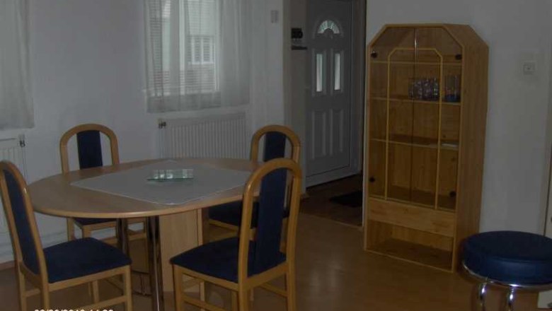 Dining area with round table, four chairs and a wooden shelf in a bright room.