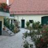A well-tended courtyard with flowers and plants, surrounded by buildings with red tiled roofs and green doors.