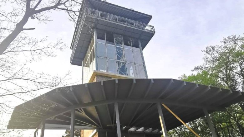Exterior view of tower cafe with glass façade and metal structure, surrounded by trees.