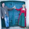 A man and a woman clink glasses of wine in front of a blue wooden door.