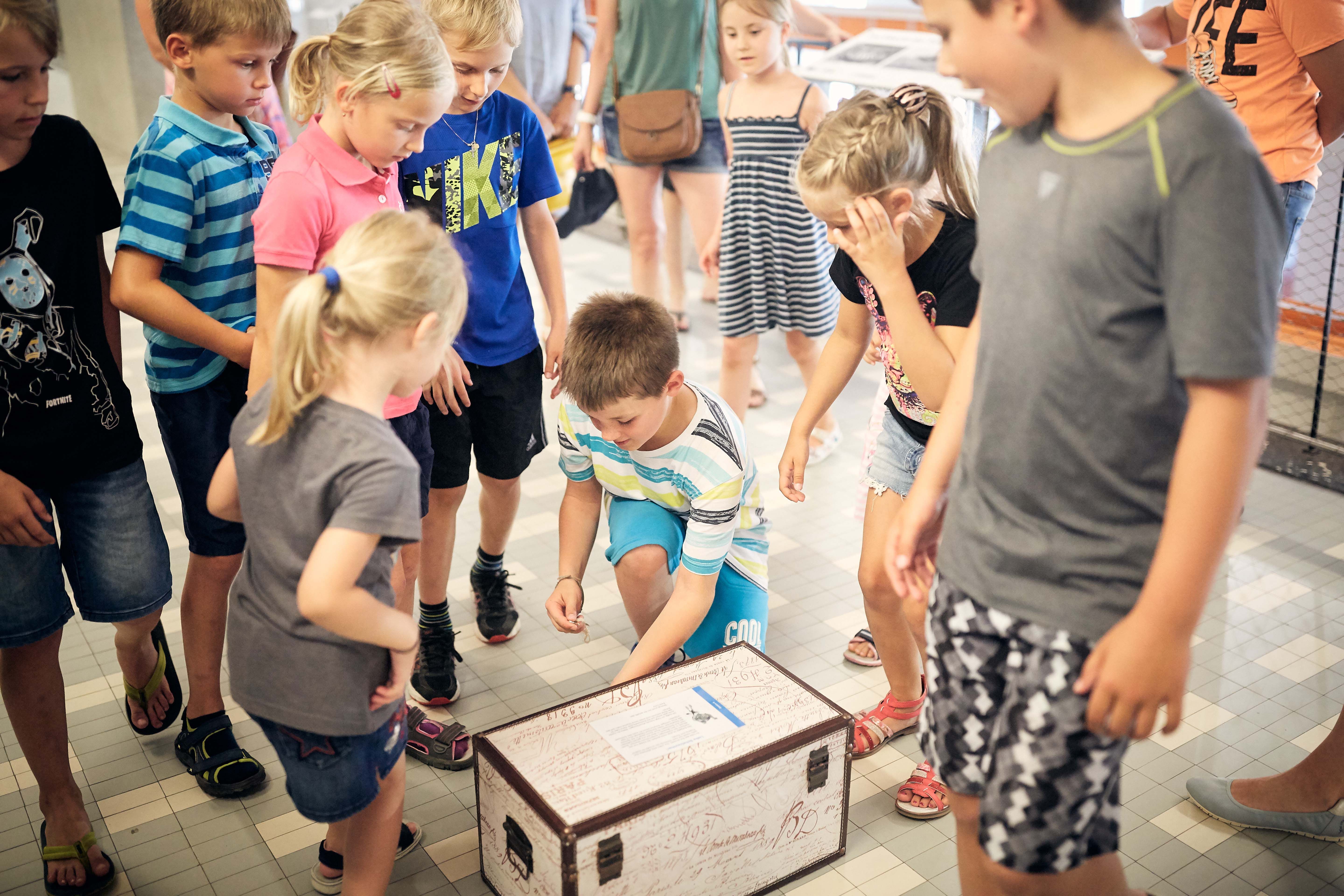 Children stand around a treasure chest lying on the floor.