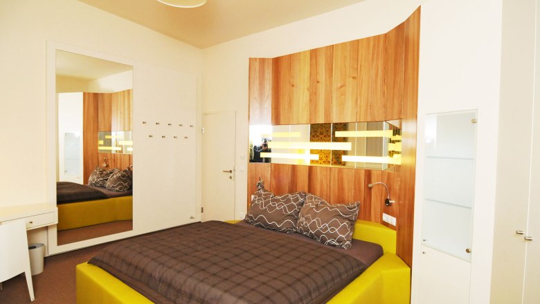 Modern furnished bedroom with yellow bed and wood paneling on the wall.