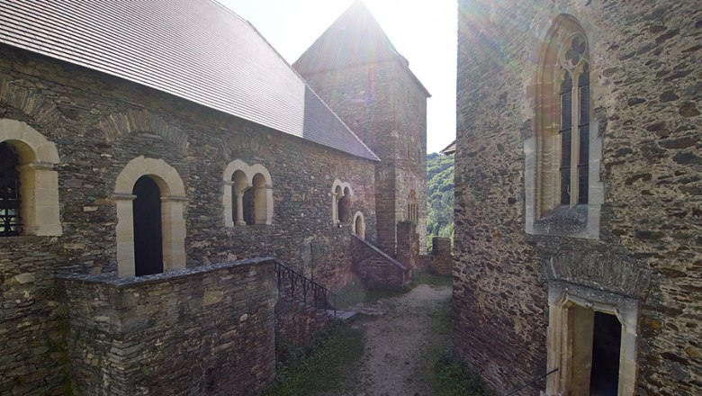 Inner courtyard of Hardegg Castle with old stone walls and Gothic windows, rays of sunshine in the background.