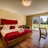 Cozy hotel room with double bed, red accents and a view of the garden through large windows.