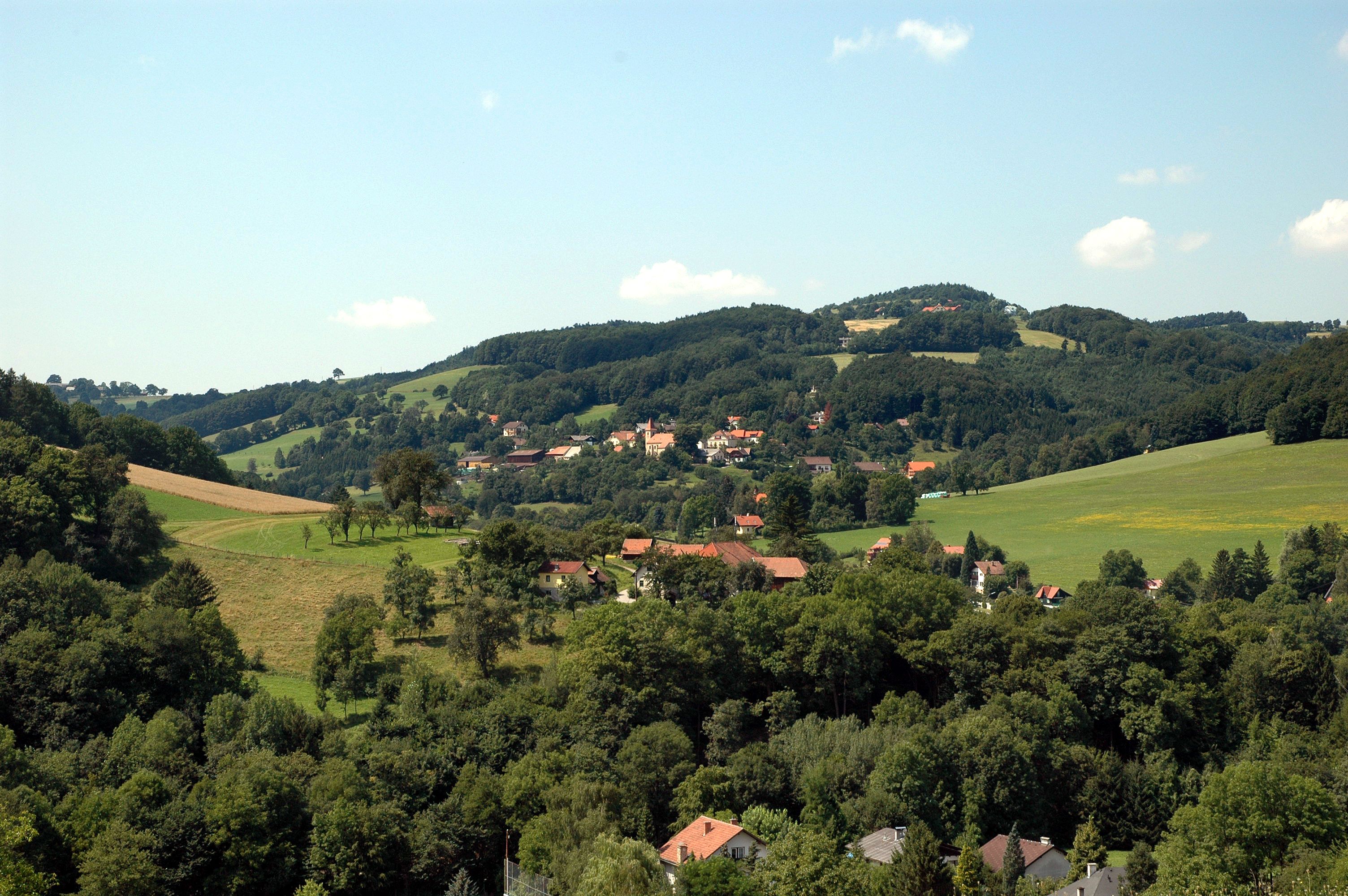 Landscape with hills, forests and a village in the background.