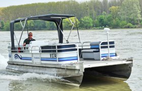 A small motorboat sails on a river, surrounded by trees on the bank.