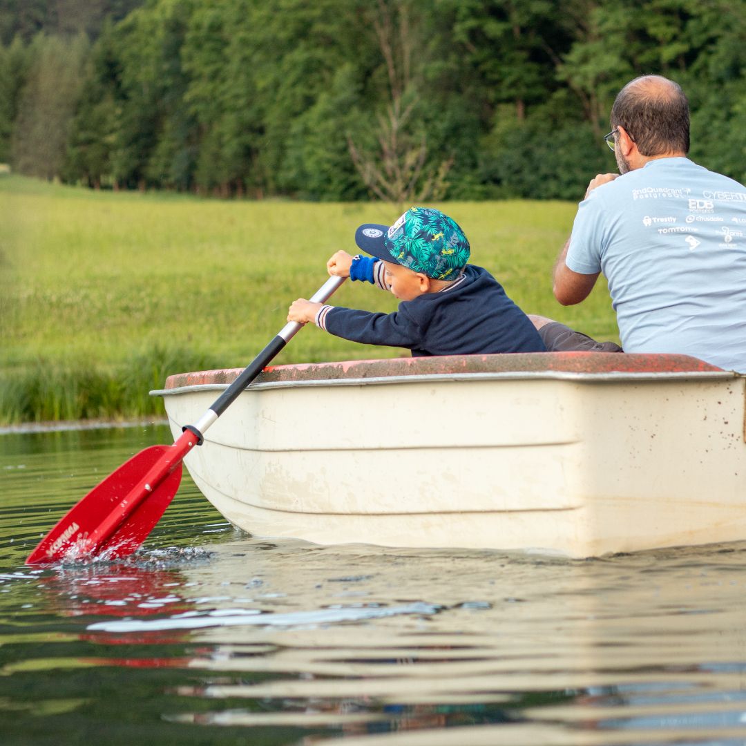 A child and an adult are rowing in a small boat on a pond.